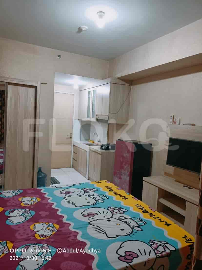 A compact bedroom with a double bed featuring a colorful Hello Kitty duvet, a mini-kitchen visible in the background, and a wardrobe.