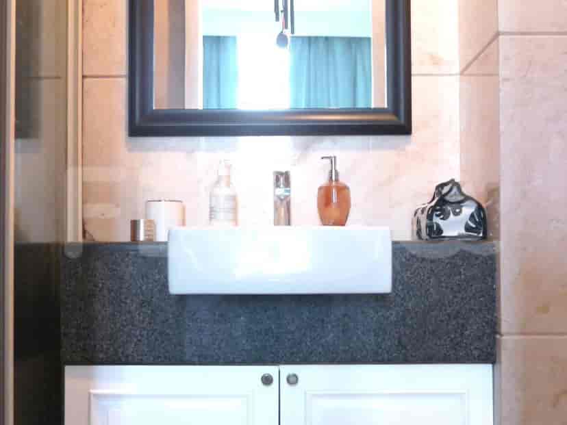 A modern bathroom with a sink, mirror, and counter space with toiletries.