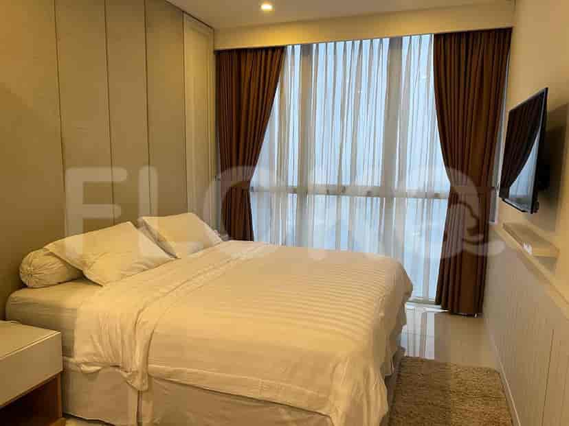A well-lit bedroom with a bed, curtains, and a mounted TV.