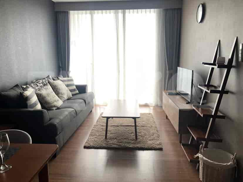 Ruang tamu modern yang menampilkan sofa abu-abu, TV, dan jendela besar.