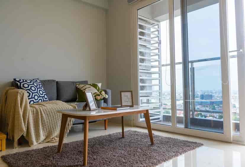 Modern living room with grey sofa, coffee table, and city view from the balcony.