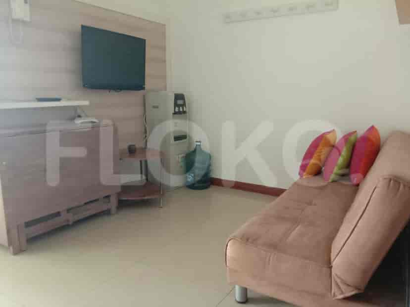 Ruang tamu kecil yang menampilkan sofa, televisi, dan dispenser air.