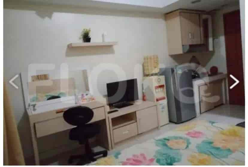 Kombinasi kamar tidur dan ruang tamu dengan meja, dapur kecil, dan TV.