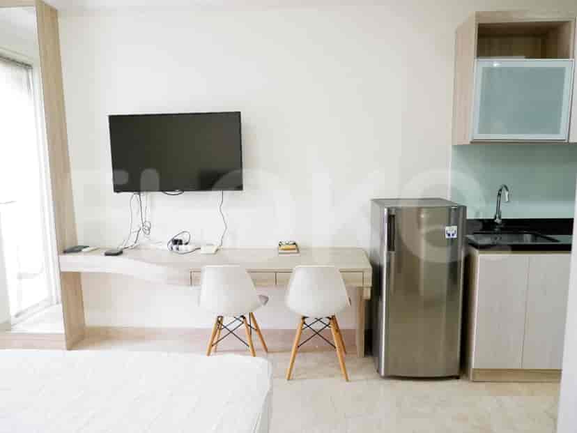 A cozy studio apartment with a bed, a small kitchen, and a refrigerator.