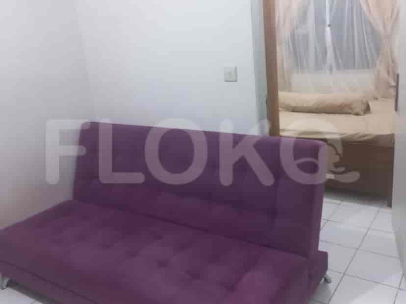 Ruang tamu yang ringkas dengan sofa bed ungu, dan pintu masuk ke kamar tidur.