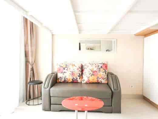 Area hidup dengan sofa abu-abu, bantal bunga, dan meja kopi merah, di bawah tempat tidur loteng.