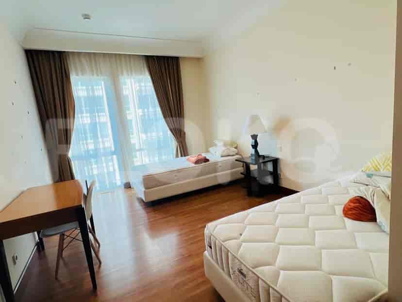 A bedroom with two beds, a desk, and large windows.