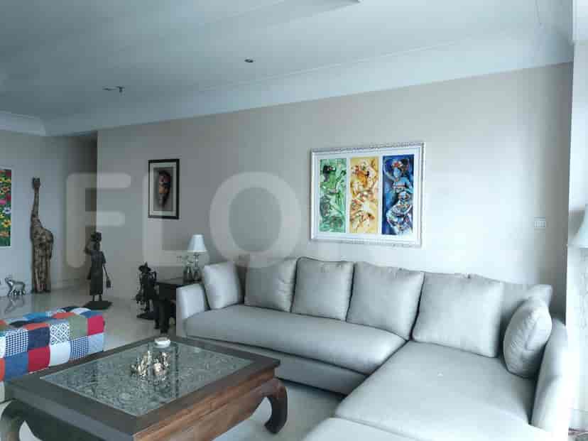 A well-lit living room with a grey L-shaped sofa, artwork, and a glass-top coffee table.