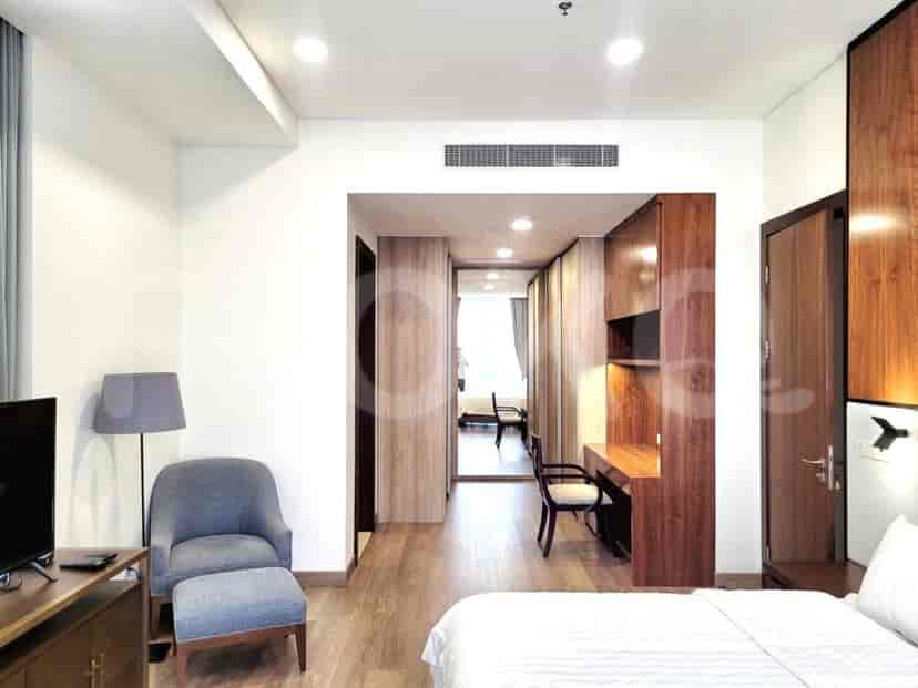 Kamar tidur dengan tempat tidur, kursi, TV, dan pemandangan ke lorong.