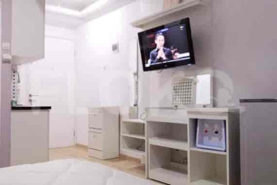 A studio apartment with a combined living area and kitchenette, featuring a TV, desk, and storage.