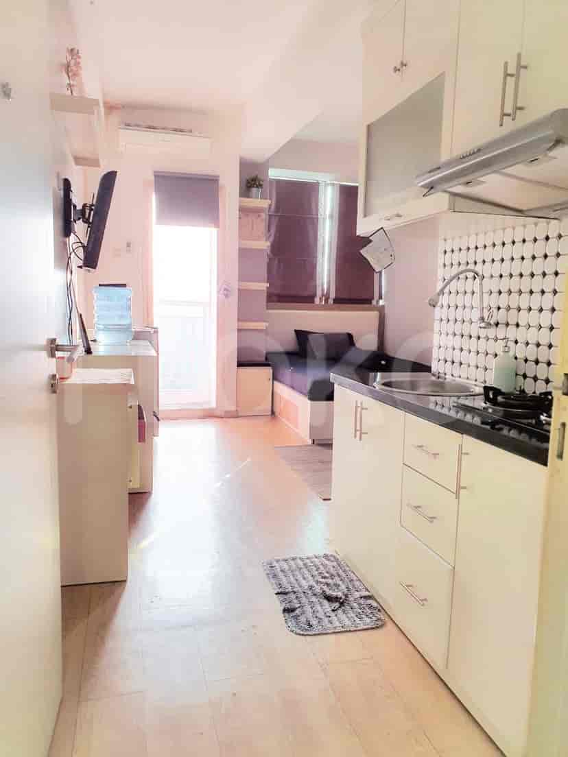 A compact living space including a small kitchen area, a water cooler and a door opening to a balcony.