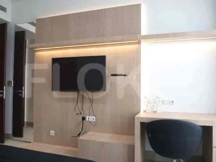 Gambar menunjukkan ruangan yang menampilkan TV yang dipasang pada panel kayu, meja dengan kursi, dan tempat tidur.