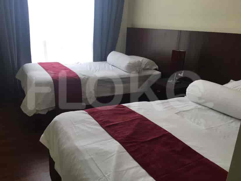 Kamar tidur modern yang menampilkan dua tempat tidur dengan aksen merah dan pencahayaan lembut.