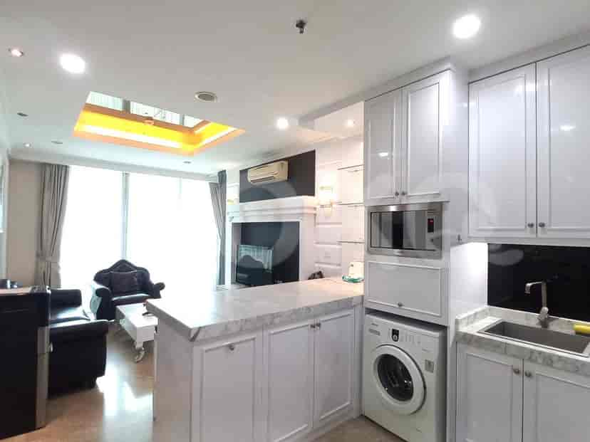 Modern kitchen with white cabinets and marble countertops, open to a living area with a black sofa.