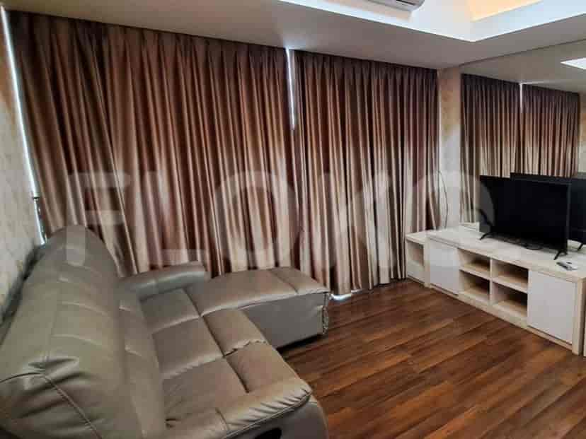 Ruang tamu modern dengan sofa berbentuk L abu-abu, TV, dan jendela besar dengan gorden coklat.
