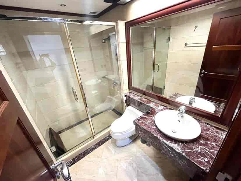 Kamar mandi dengan pancuran kaca, toilet putih, dan meja coklat.