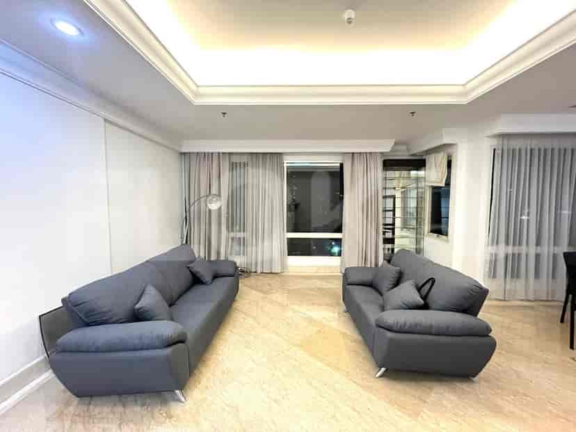 Ruang tamu luas dengan dua sofa abu-abu, lantai marmer, dan jendela besar.