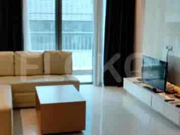 Ruang tamu modern dengan sofa berbentuk L berwarna krem, TV yang dipasang di dinding, dan pintu kaca geser yang mengarah ke balkon.