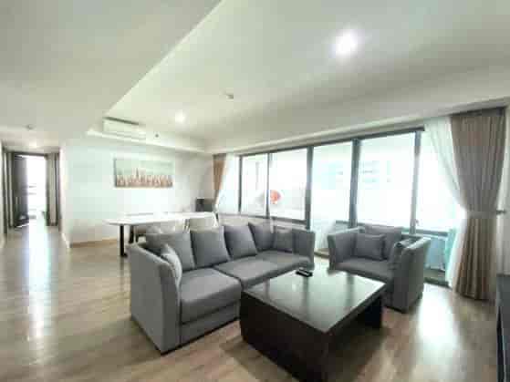 A spacious living room with an L-shaped grey sofa, a coffee table, and a large window with sheer curtains.