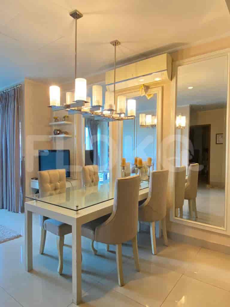 An elegant dining room with a glass table, comfortable chairs, a large mirror, and a chandelier.