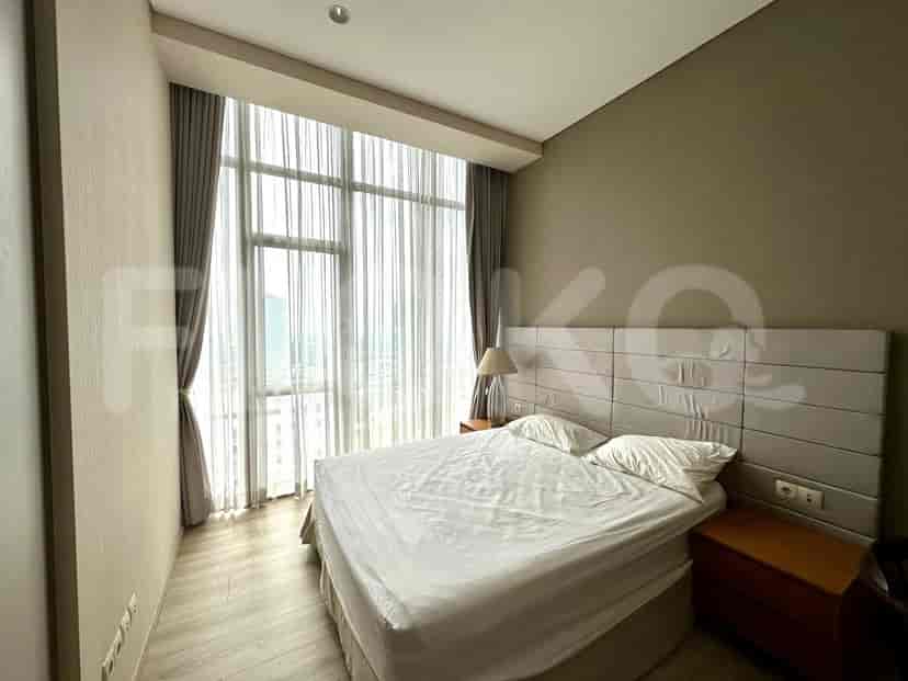 A bedroom with a bed, large window with sheer curtains, and a bedside table with a lamp.