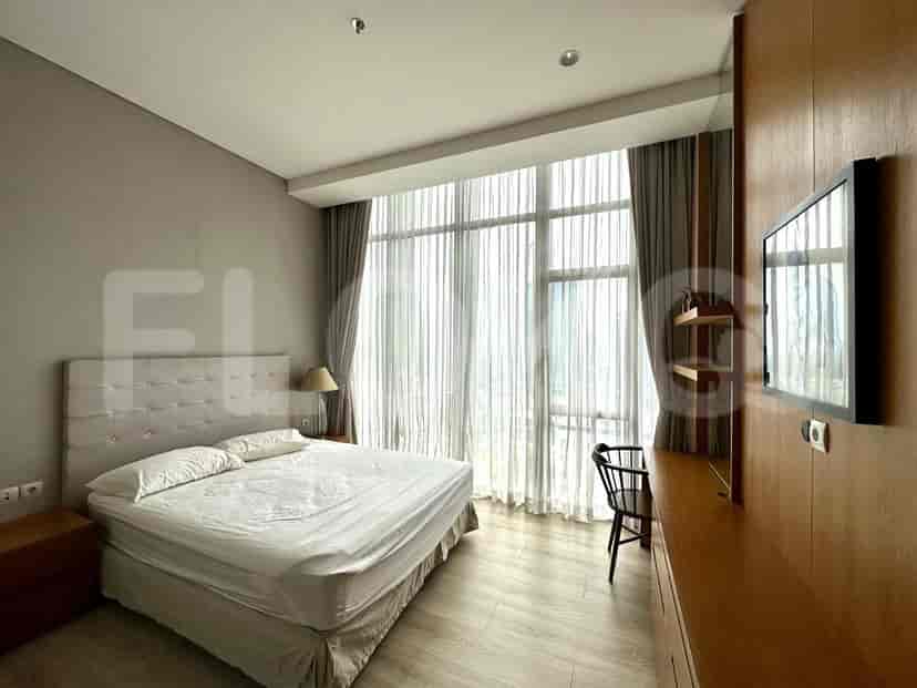 A bedroom with a bed, a bedside table, and a TV, with a view through a large window.