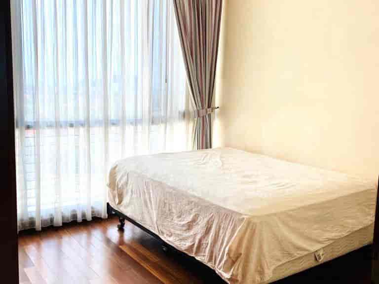 A bedroom with a bed, curtains, and hardwood flooring.