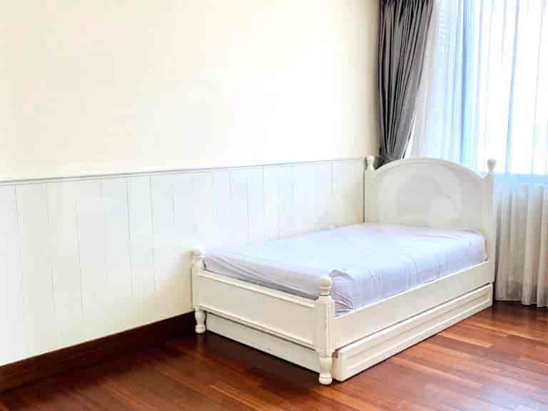 A bedroom with a white bed, wood paneling, and hardwood flooring.