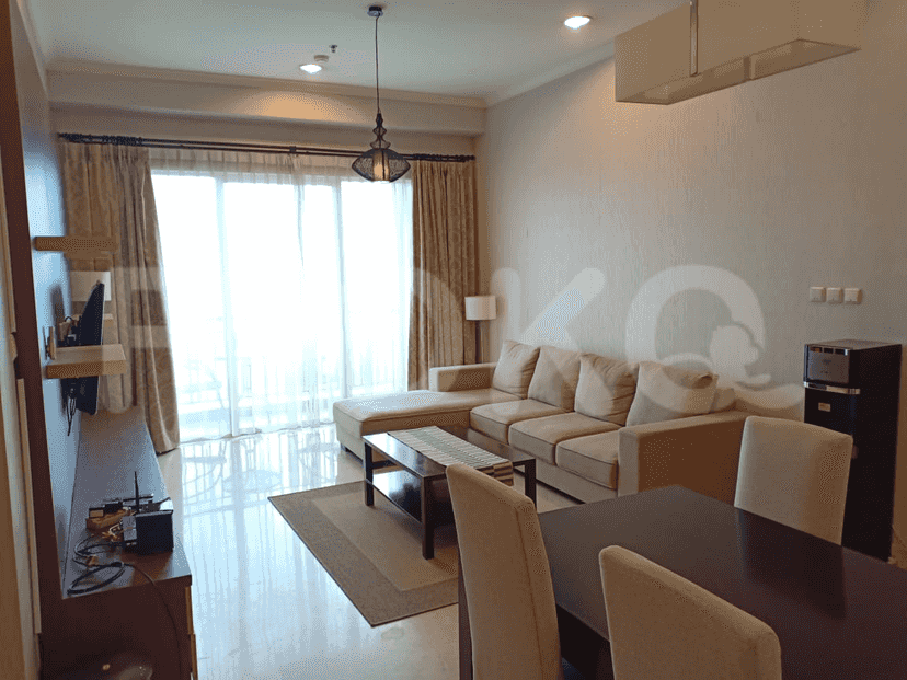 A living room with a beige L-shaped sofa, a dark wood dining table, and a large window with sheer curtains.