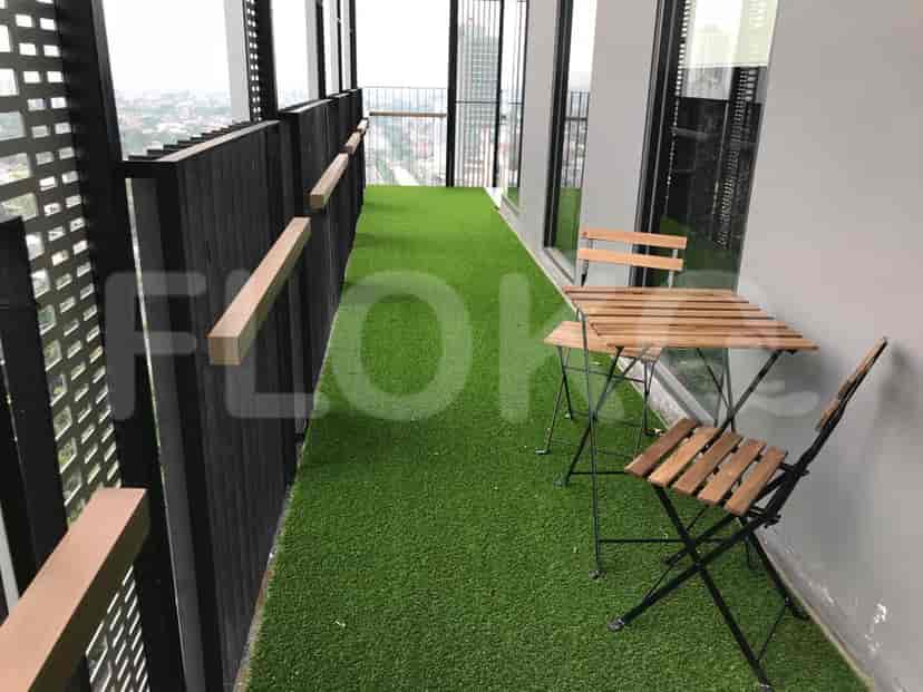 A small balcony with synthetic grass, wooden chairs, and a table.