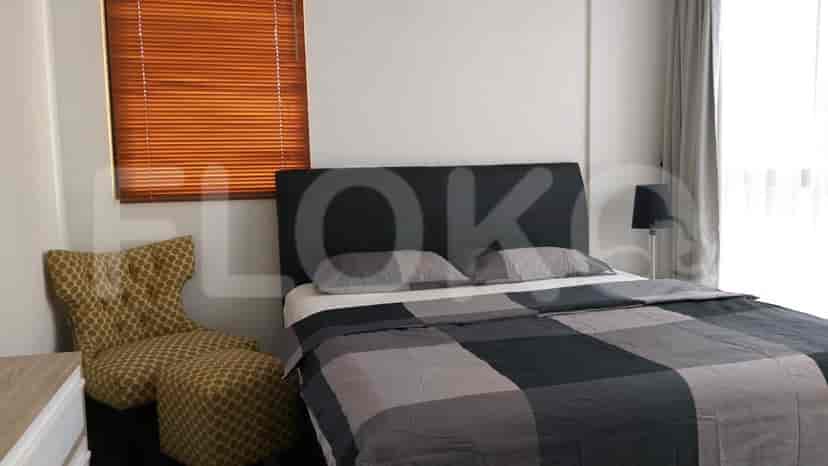 A bedroom with a queen bed, patterned chair, and wooden blinds.