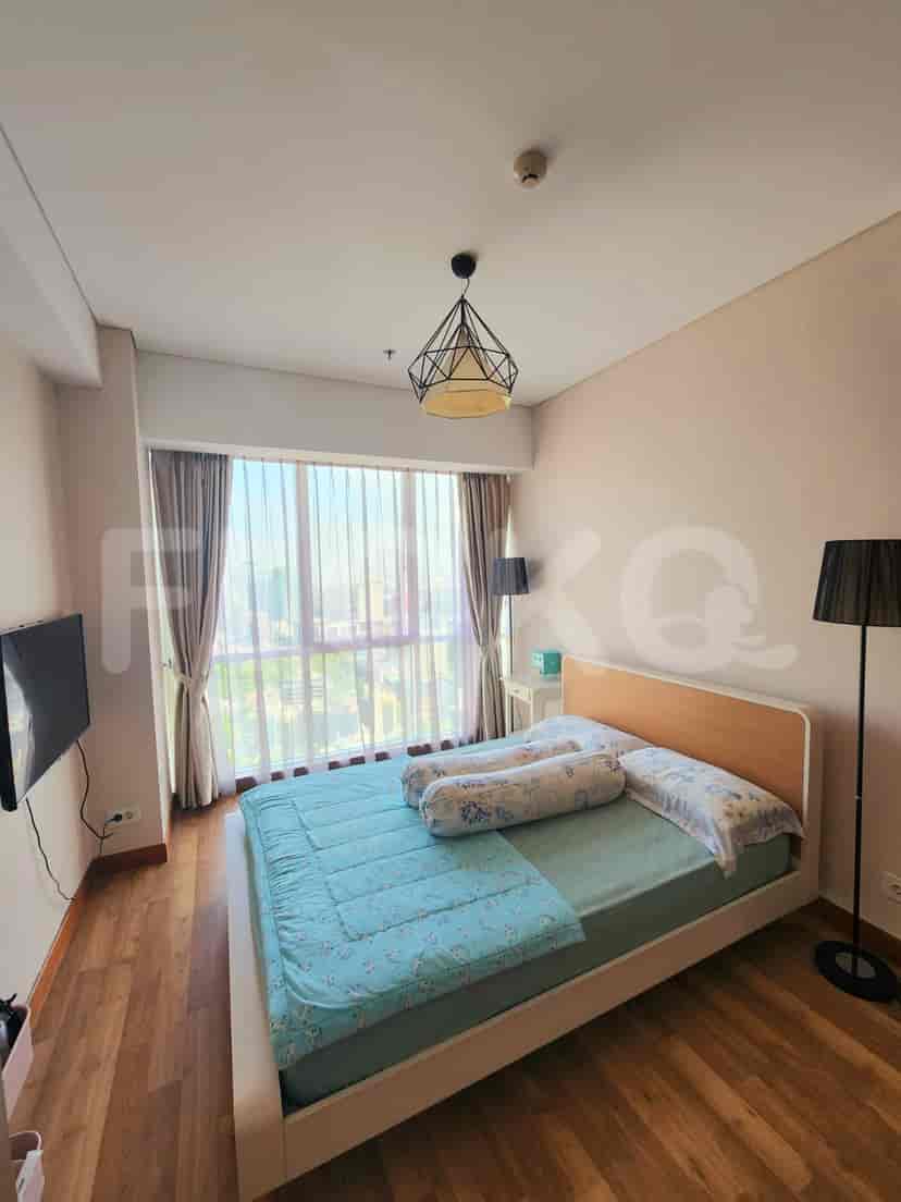 A well-lit bedroom featuring a bed with blue bedding, a large window, and a stylish ceiling lamp.