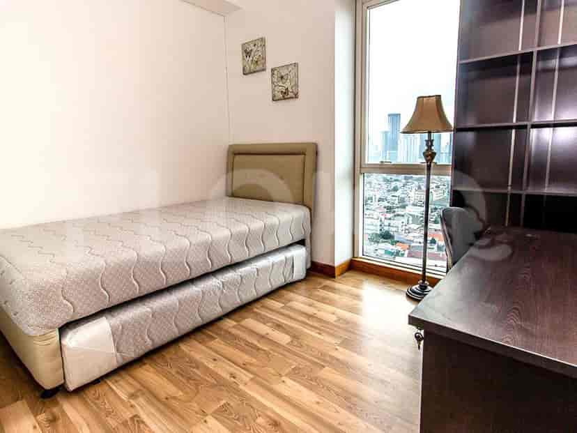 A bedroom with a single bed and a desk, alongside large windows offering a cityscape view.