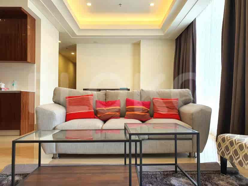 A modern living room featuring a grey sofa with colorful cushions, glass coffee tables, and dark curtains.