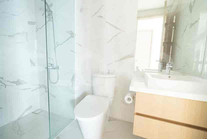 Modern bathroom with a glass shower, marble walls, and wooden vanity.