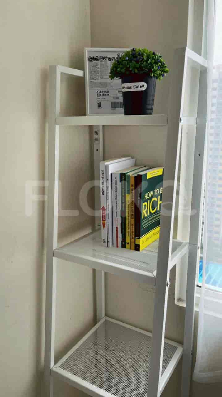 Rak putih yang menampilkan buku dan tanaman.