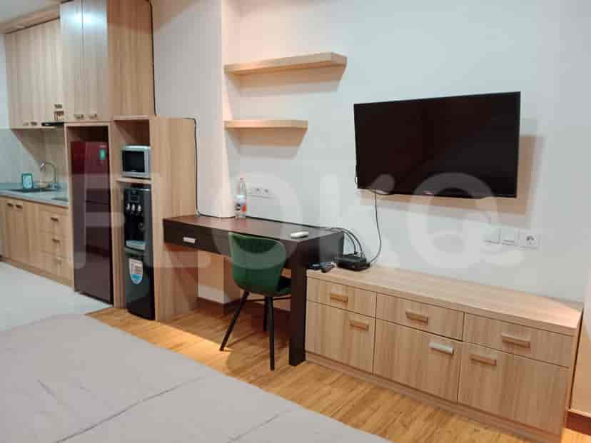 A combined living and kitchen area with a desk, kitchen appliances, and a wall-mounted TV.