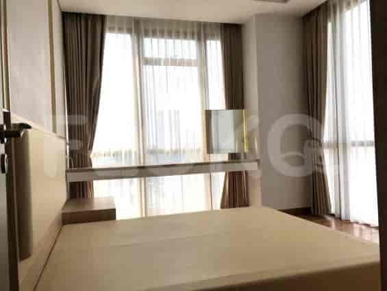 A well-lit bedroom with a large window, neutral-toned bedding, and a built-in desk/console.