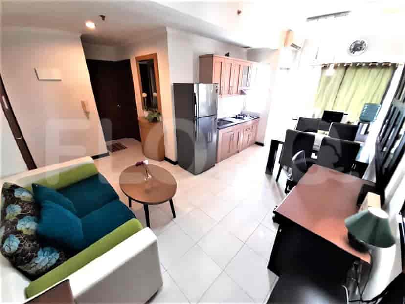 Ruang tamu dengan sofa teal, meja kopi bundar, dan pintu masuk ke rumah.