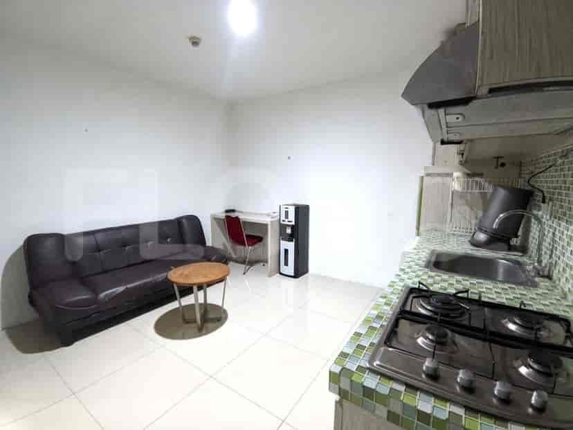 A living space featuring a brown leather sofa, a round wooden coffee table, and a compact kitchen setup.