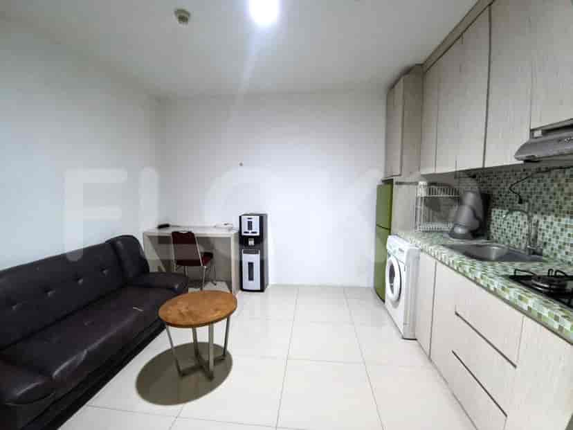 A living area with a brown leather sofa, a round wooden coffee table, and a compact kitchen setup, including a washing machine and a refrigerator.