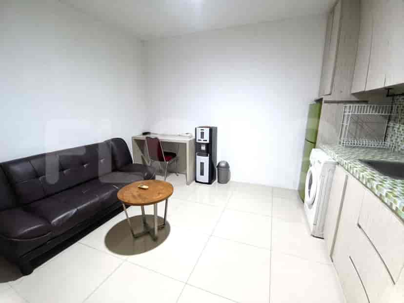 A living area with a brown leather sofa, a round wooden coffee table, and a compact kitchen setup.