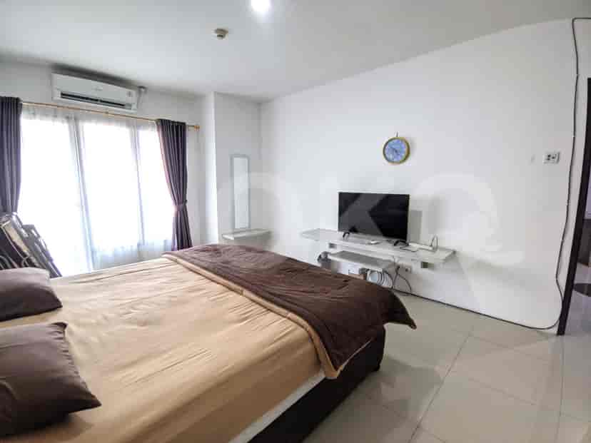 A bedroom with a double bed, a wall-mounted TV, and a window with purple curtains.