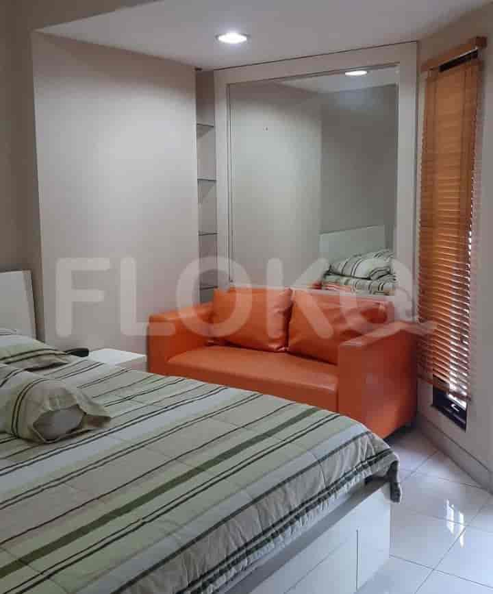 A cozy bedroom with a bed, small orange sofa, and large mirror.