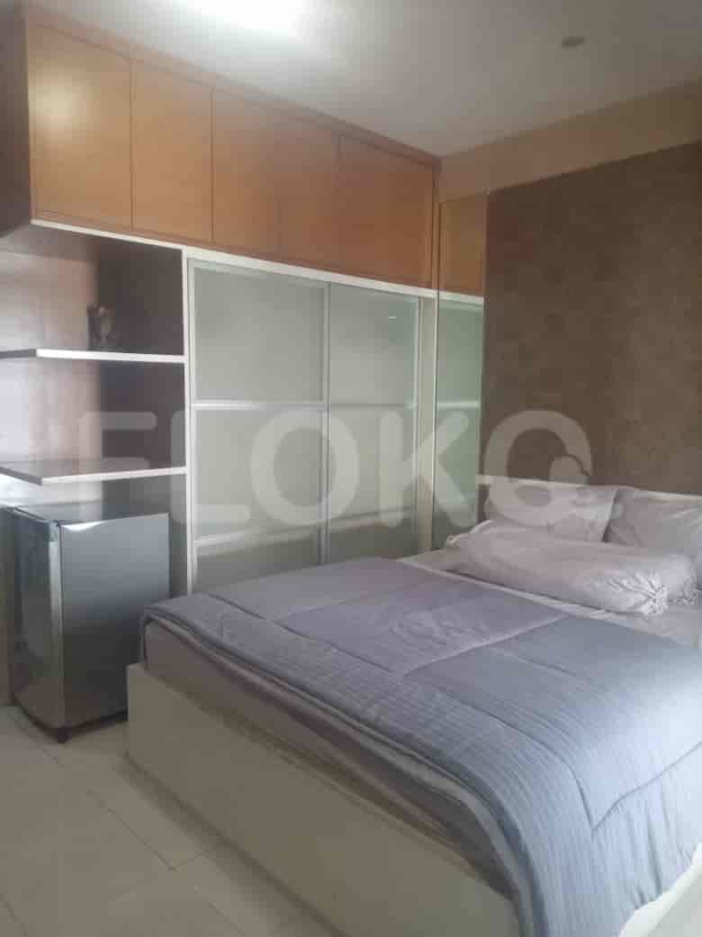 A bedroom with a bed, a small fridge, and wooden cabinets.