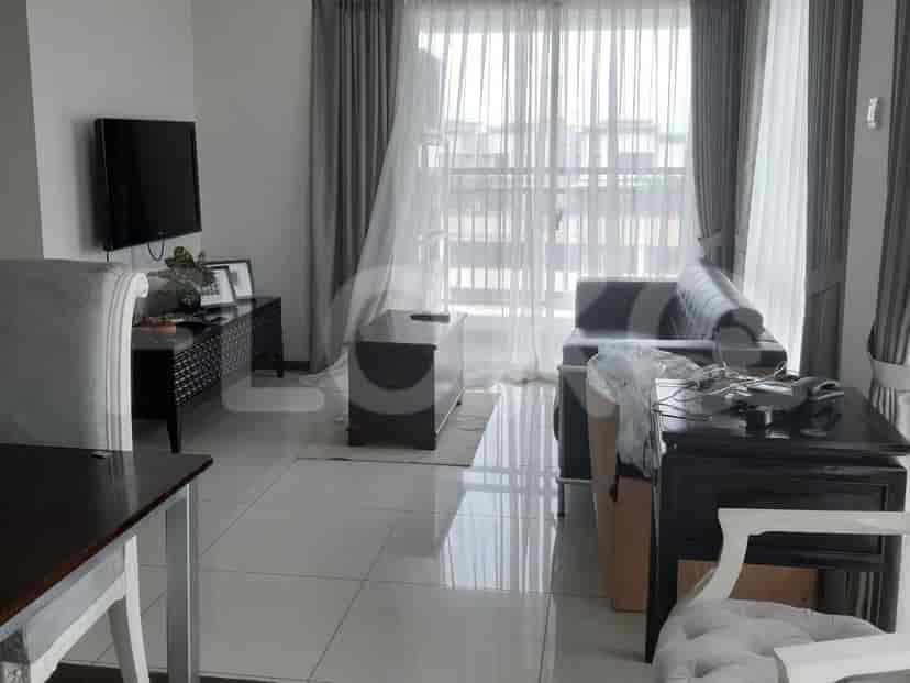 A living room with a grey sofa, a TV, a coffee table, and large windows.