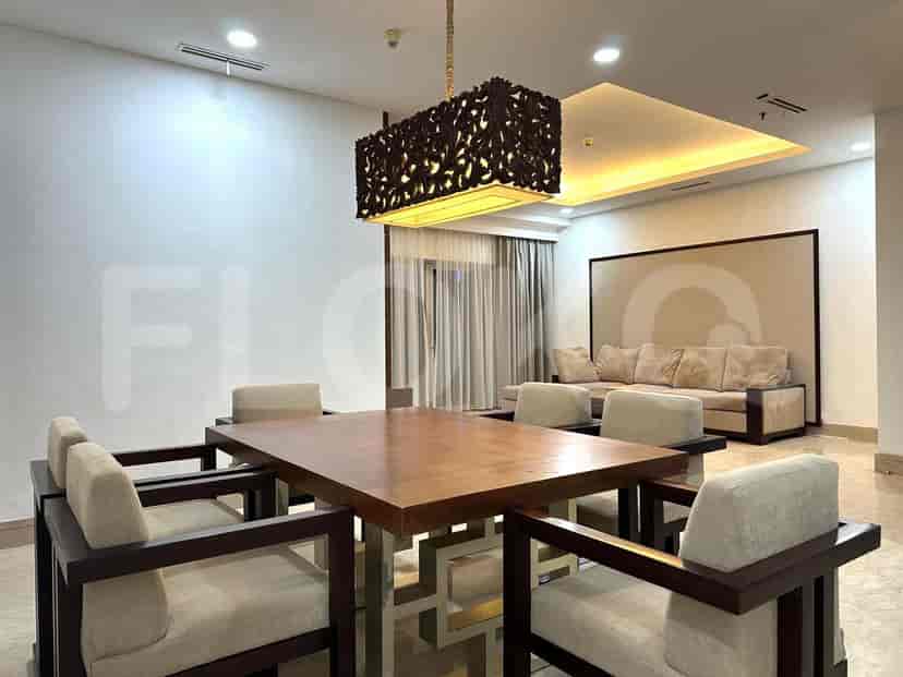 Meja makan dengan kursi, sofa, dan dapur di latar belakang.