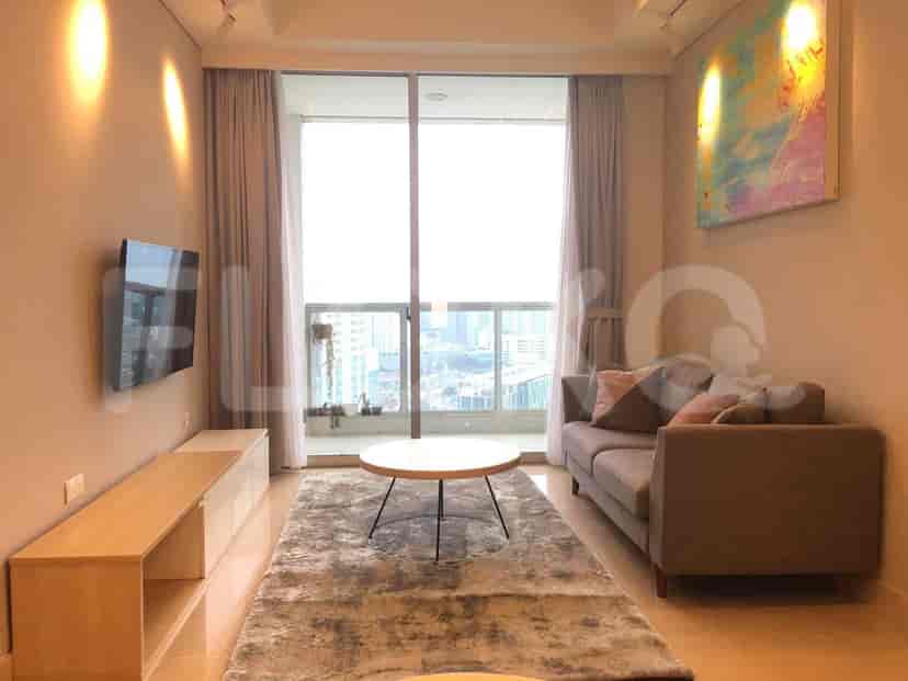 A modern living room with a sofa, TV, and city views through large windows.
