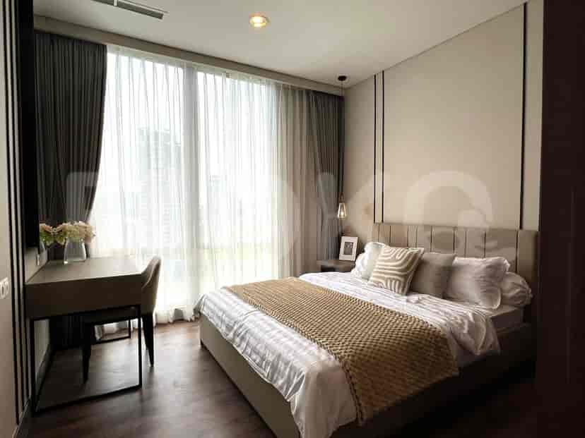 A bedroom with a bed, desk, and large windows with sheer curtains.
