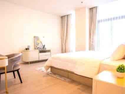A well-lit bedroom with a large bed, a bedside table, and a vanity area.